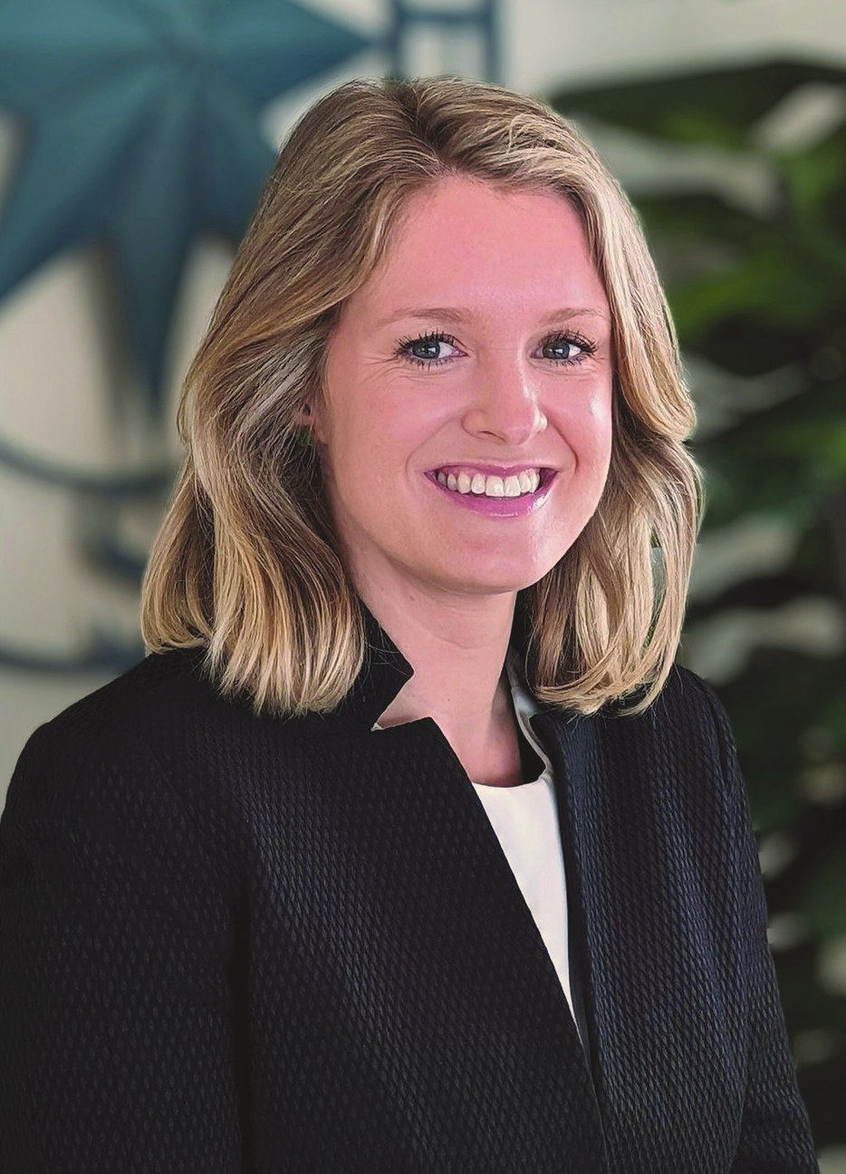 Dora O'Donoghue in a black jacket, smiling, against a leafy background