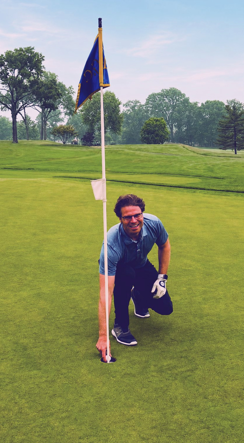 Tom Reichart kneeling on a putting green, retrieving a ball from the hole