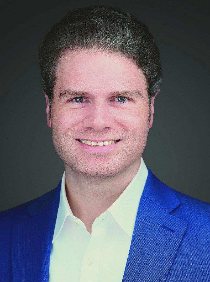 Tom Reichart in a blue suit jacket against a dark background